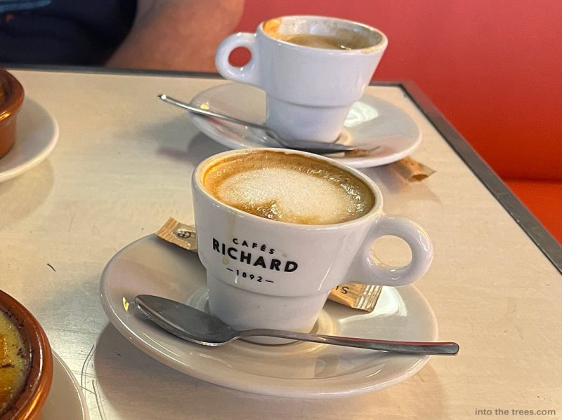 Two small cups of coffee on saucers with spoons.